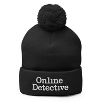 Black pom-pom beanie with Online Detective embroidered artwork, front view