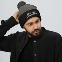Black pom-pom beanie with Online Detective embroidered artwork, front view