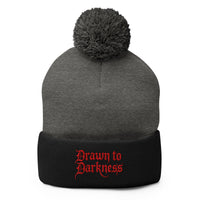 Black pom-pom beanie with Drawn to Darkness embroidered artwork, front view