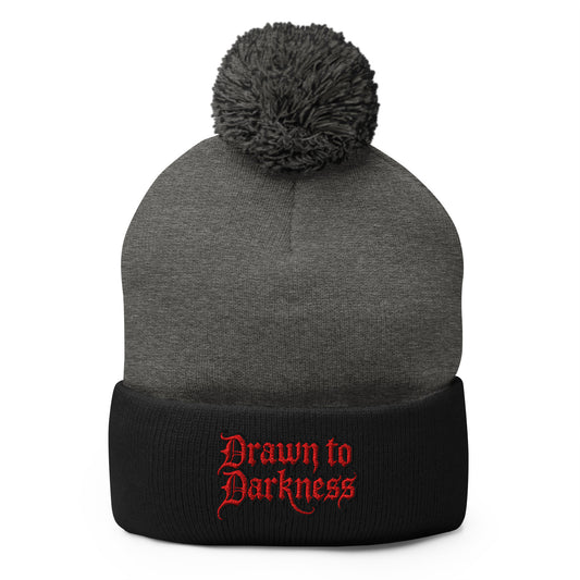 Black pom-pom beanie with Drawn to Darkness embroidered artwork, front view