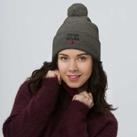 Gray pom-pom beanie with True Crime Blood Drop embroidered artwork, front view